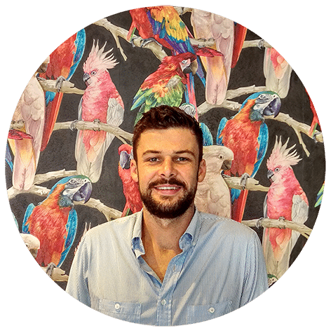 A man in front of a painting of cockatoos and parrots