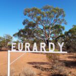 White sign that reads EURARDY, in front of trees with clear blue sky.