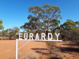 White sign that reads EURARDY, in front of trees with clear blue sky.