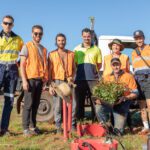 Seven people in high-vis clothing standing in front of a ute, with seedlings and planting tools.