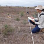 Woman kneeling in planting area writing on a piece on paper