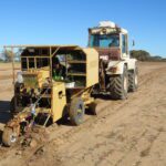 Tractor towing a trailer driving across a sandy paddock.