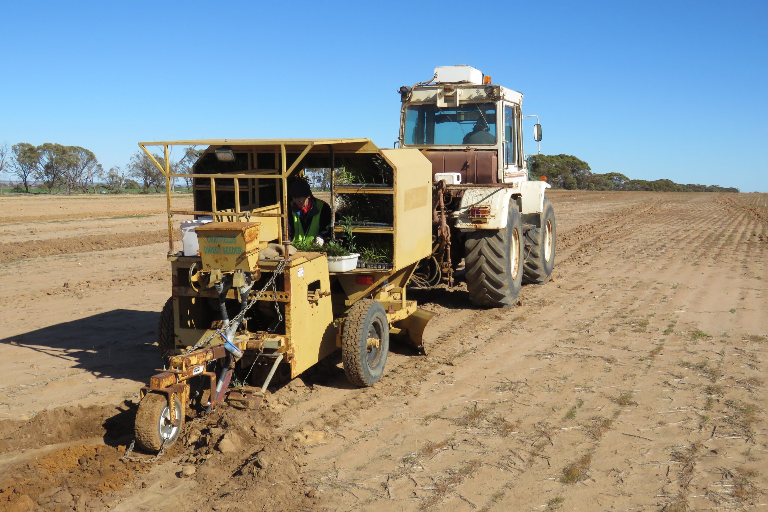 Tractor towing a trailer driving across a sandy paddock.