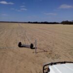 Photo of a sandy paddock with a roll of fencing wire on the ground in front of a white ute bonnet.