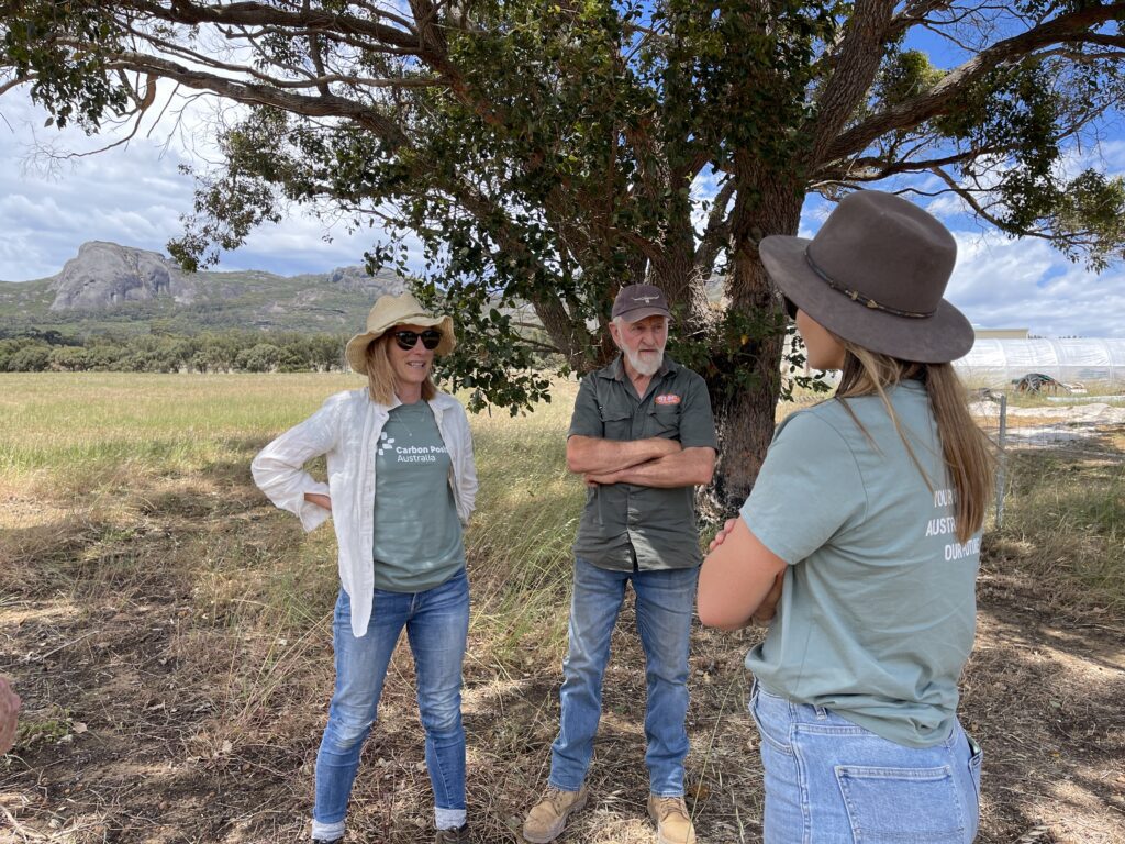 Three people standing underneath a tree in a paddock with ranges in the background