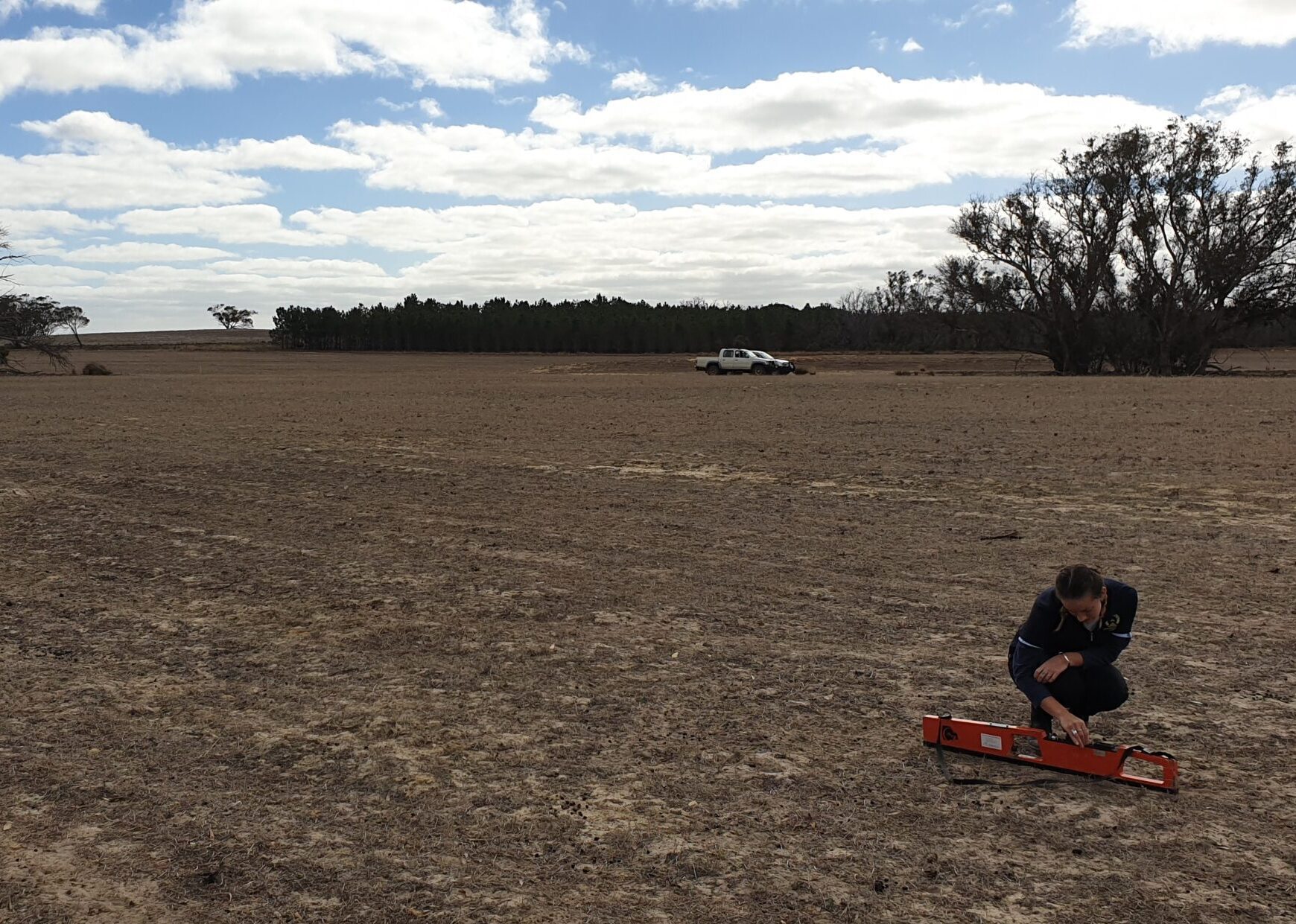 Woman bending down in bare field measuring soil salinity