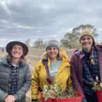 Three women smiling in front of a paddock
