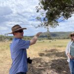 Man pointing in a bare paddock with mountain range in the background