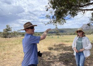 Man pointing in a bare paddock with mountain range in the background