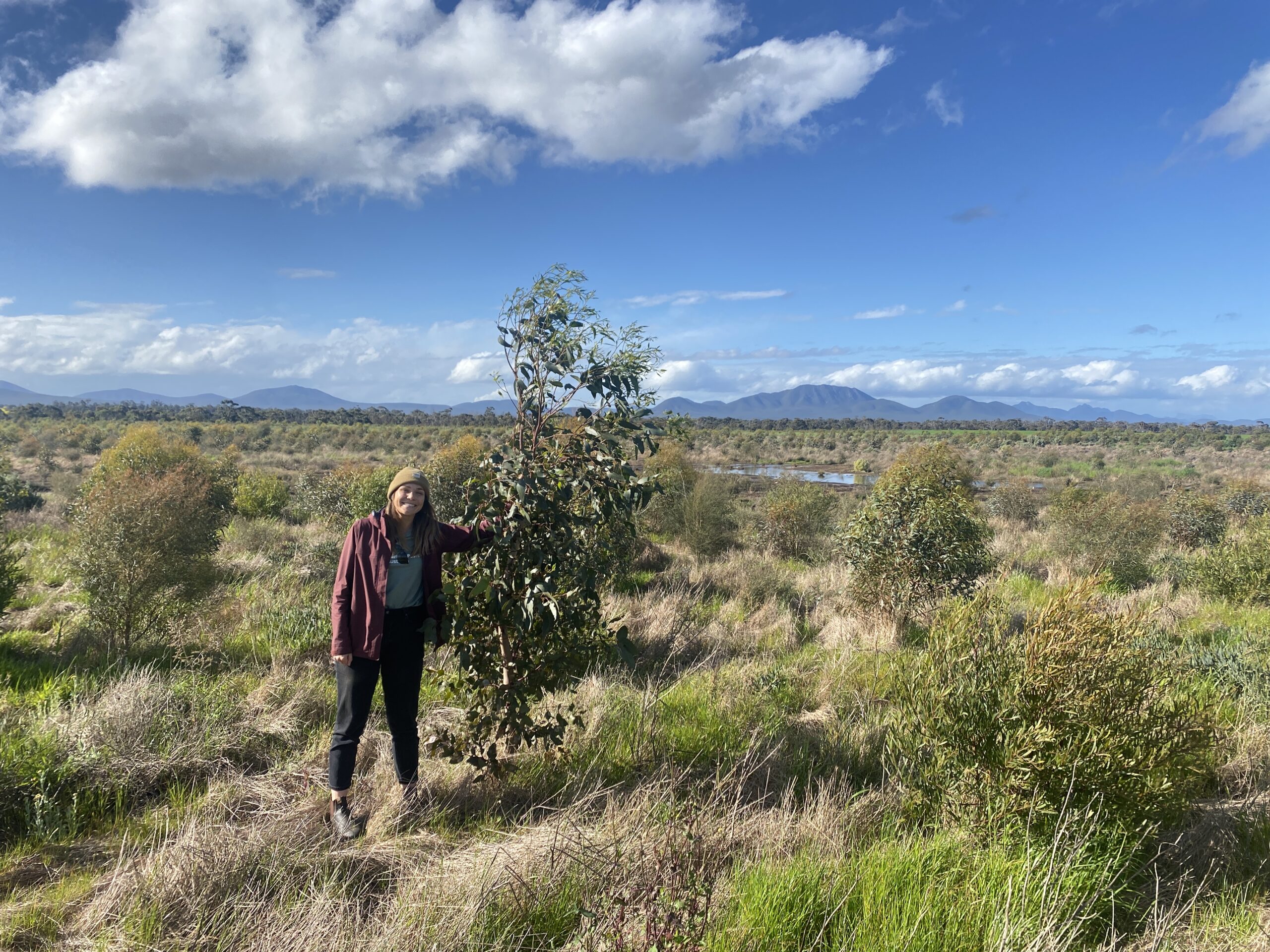 Woman standing next to a small tree in a paddock