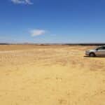 Cleared area of flat land with sandy yellow soil and silver car