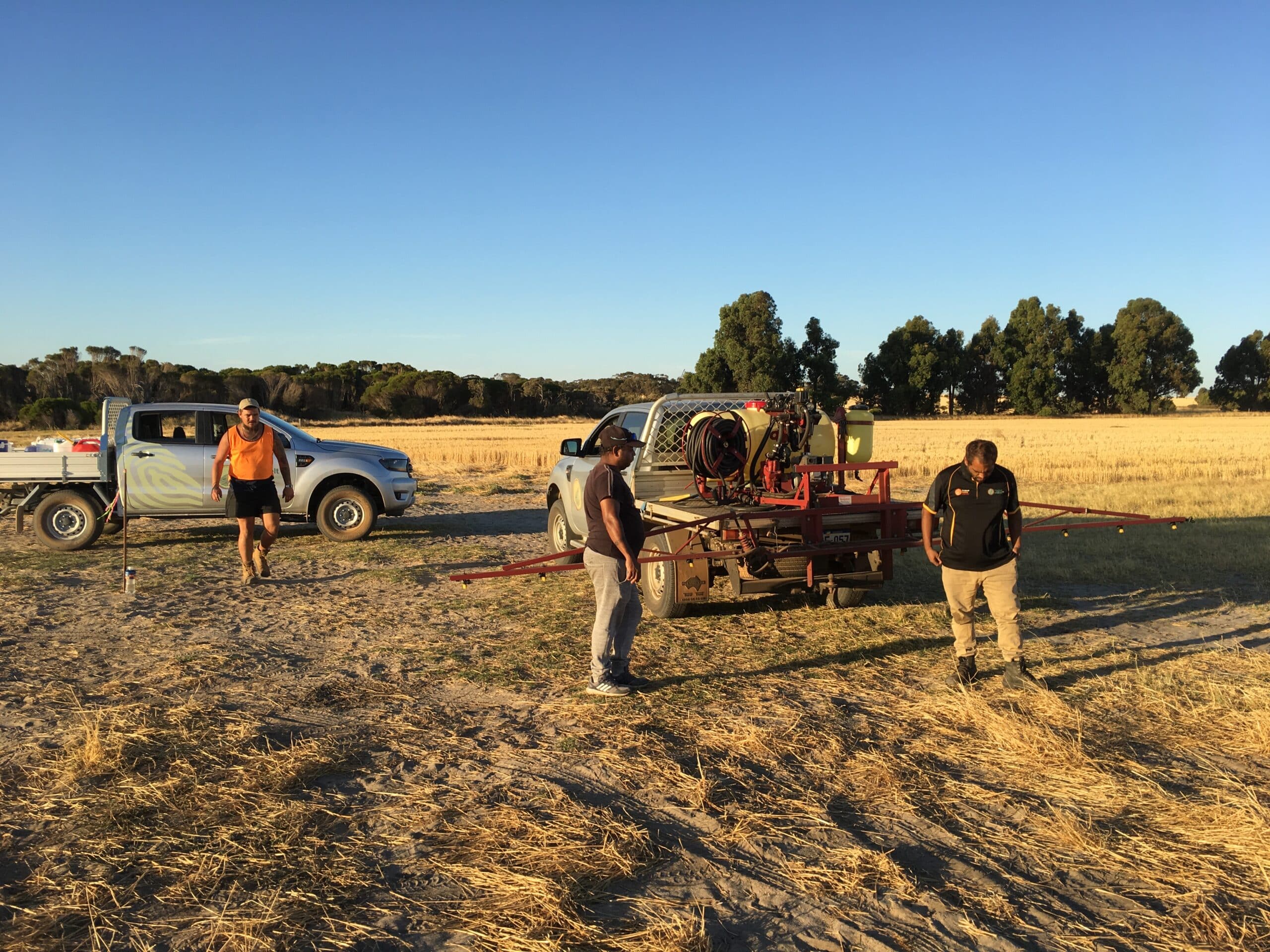 Three men standing next to 2 cars in the planting area ready for site preparation. 