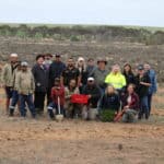 Group photo of 19 people with seedlings buckets standing in a cleared area