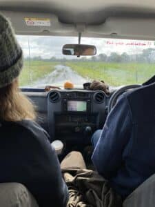 Two people sitting in the front seats of a car driving on a dirt road