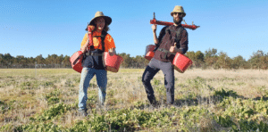 Two men posing with planting buckets and devices.