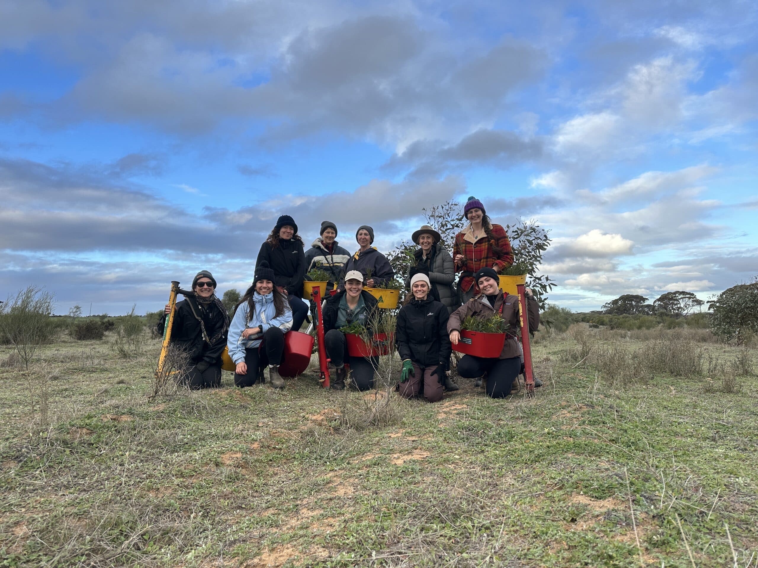 Group photo of ten woman standing and crouching in a field with pottiputki's and seedings buckets