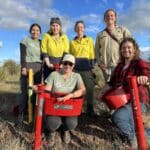 Group photo of 6 people smiling with seedling planters and buckets.