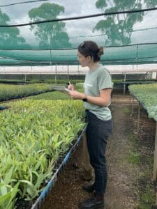 Lady holding a clipboard inspecting rows of seedlings