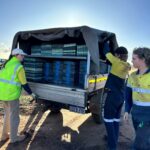 Three people standing around a ute full of empty seedling trays