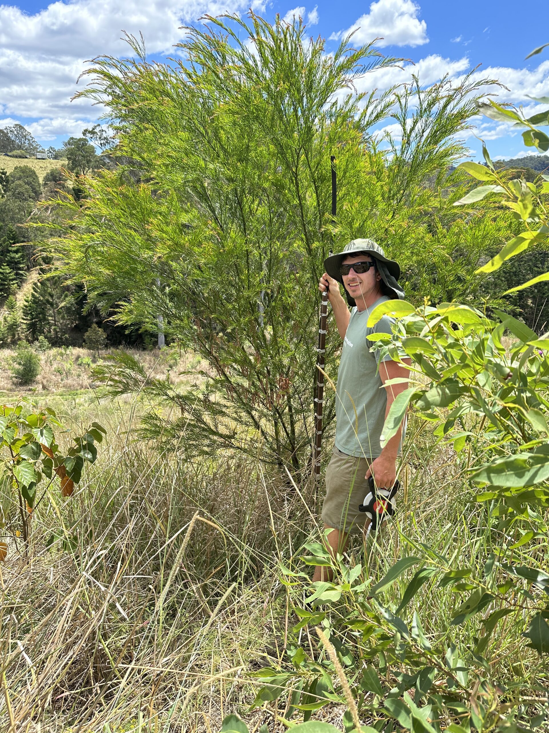 man smiling standing next to a tree holding a measuring stick