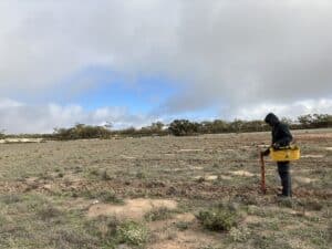 Person wearing a black hoodie using a tree planting device to plant native trees in a bare field