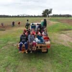 Children and Adults sitting on the back of a cart tray in an open paddock