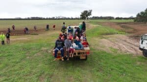 Children and Adults sitting on the back of a cart tray in an open paddock