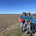 Three women standing and smiling in the middle of a paddock