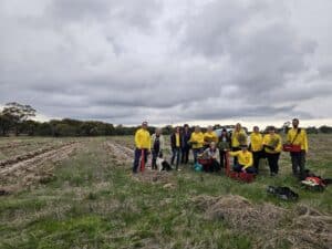 Group photo of people standing together in an empty field with planting rows. 