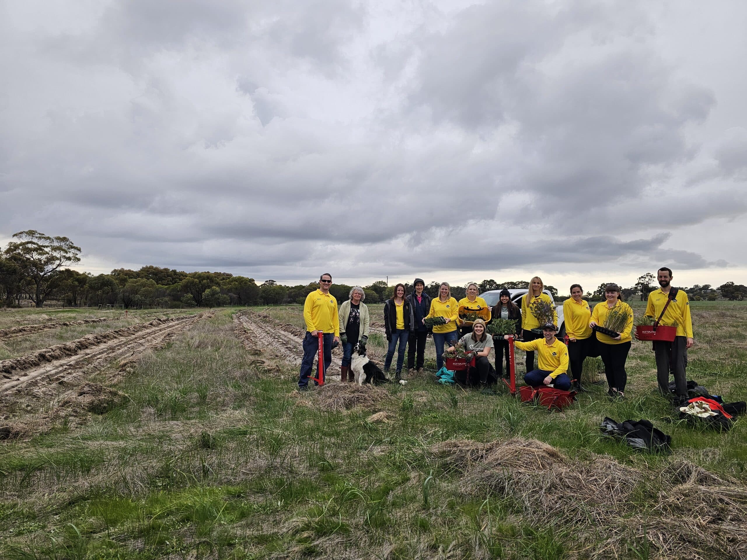 Group photo of people standing together in an empty field with planting rows.