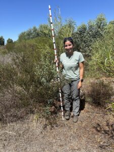 Woman holding monitoring stick and standing next to vegetation growth